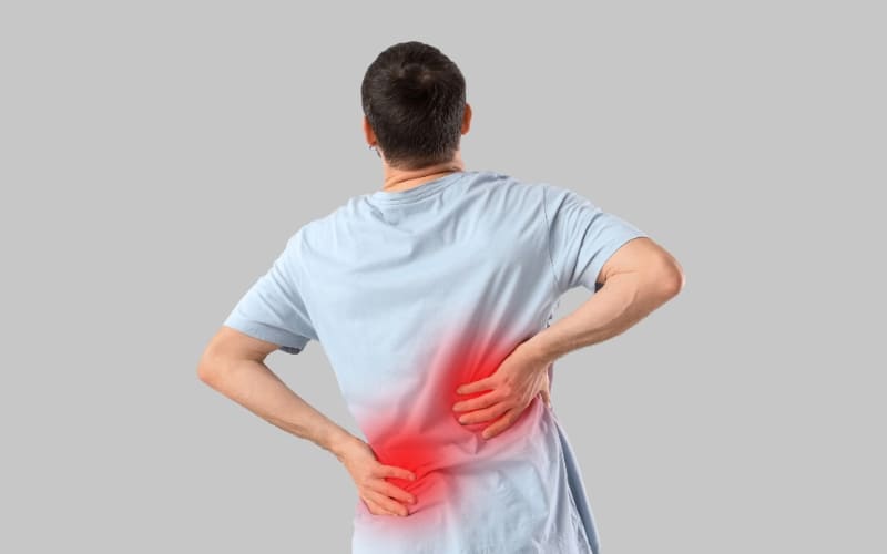 Man holding his lower back in pain while consulting a physiotherapist for persistent back pain treatment in a clinic.